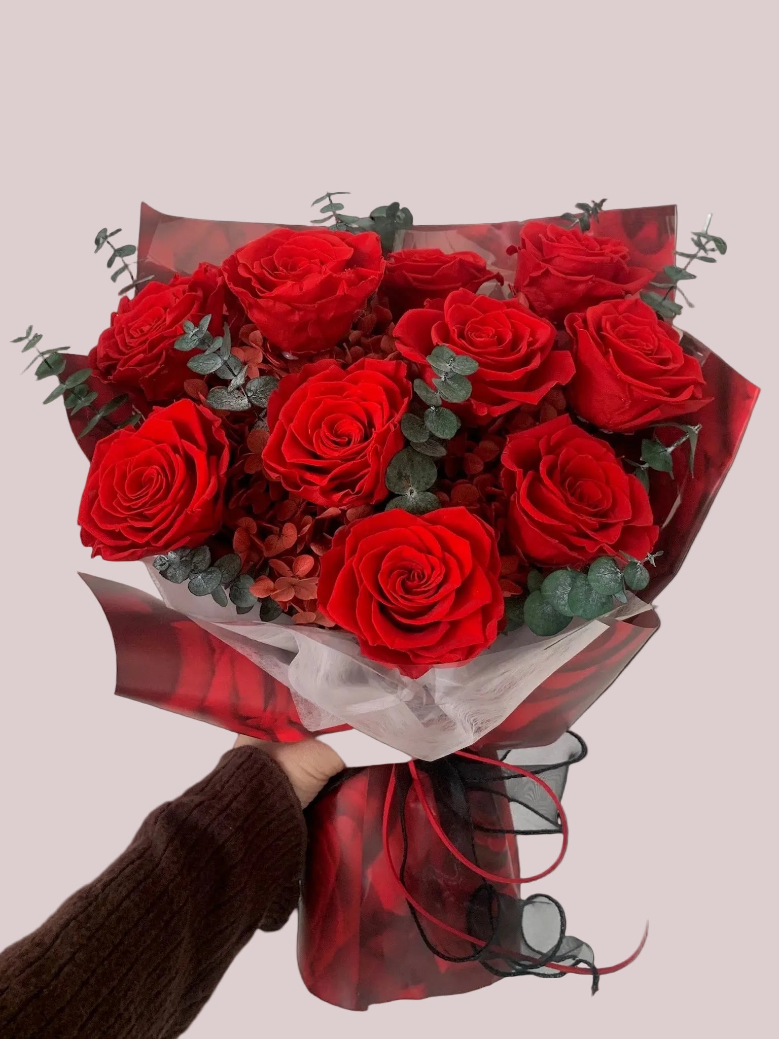 Bouquet of red roses held by a person against a plain background